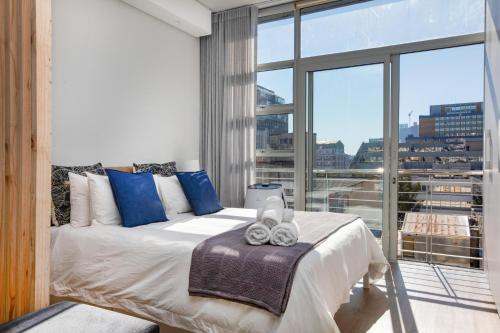 um quarto com uma cama com almofadas azuis e uma grande janela em Backup-Powered Trendy NY City Apartment at Table Mountain em Cidade do Cabo