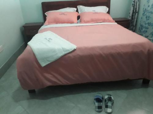 a bed with pink sheets and pillows and a pair of shoes at Kyato Hotel in Kasanda
