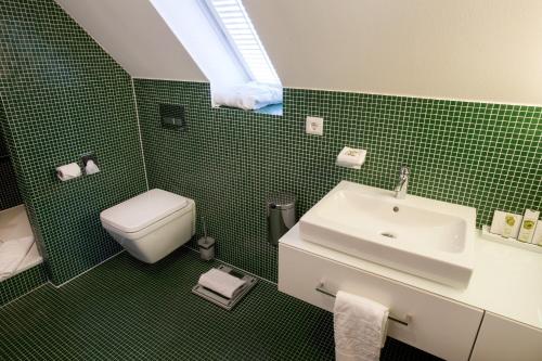 a green tiled bathroom with a sink and a toilet at Schlosshotel Hugenpoet in Essen