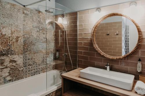 a bathroom with a sink and a mirror and a tub at Baya Hotel in Capbreton