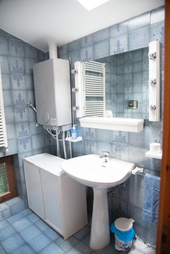 La salle de bains est pourvue de carrelage bleu, d'un lavabo et d'un miroir. dans l'établissement Appartamento Le Betulle, à Erbezzo