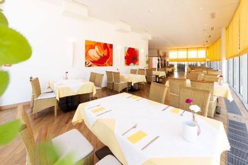 um restaurante com mesas e cadeiras brancas e pinturas na parede em Business Hotel Ambio Gleisdorf em Gleisdorf