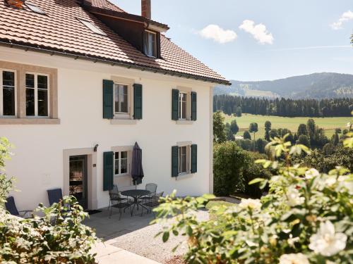 a white house with a patio with a table and chairs at Jurabelle in La Côte-aux-Fées