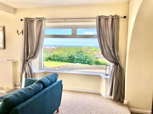 a living room with a blue couch and a large window at Bodarfor in Trearddur