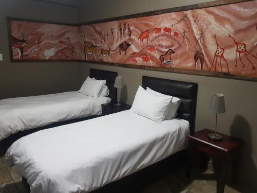 two beds in a hotel room with a painting on the wall at Hotel Portao Diaz in Mossel Bay