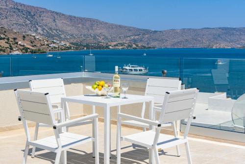 a white table with a bottle of wine and a bowl of fruit at Naiades Village Elounda in Elounda