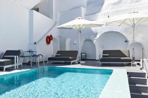 a swimming pool with chairs and umbrellas in a building at Filotera Suites in Oia