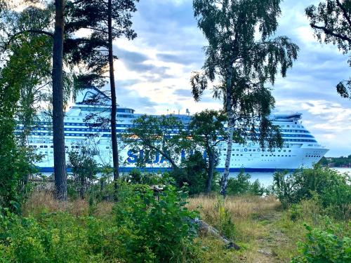 a large cruise ship in the water with trees at Charmig stuga av rustik stil i Stockholms område in Stockholm