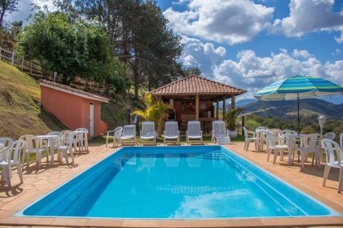 a pool with chairs and an umbrella and a gazebo at Pousada Sonho Meu in Itanhandu