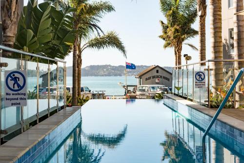 a swimming pool with palm trees and the water at Edgewater Palms Apartments in Paihia