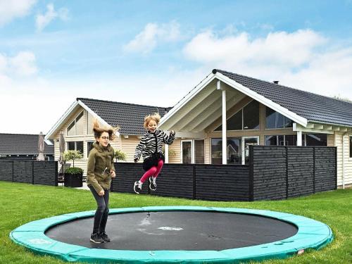 18 person holiday home in Bogense في بوجنسي: طفلين يقفزون على الترامبولين امام المنزل