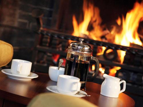 a coffee pot on a table with cups and a fireplace at voco Letchworth Hall by IHG in Letchworth