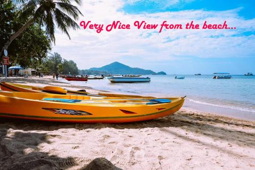 a yellow kayak on a beach with boats in the water at Wind Beach Resort in Koh Tao