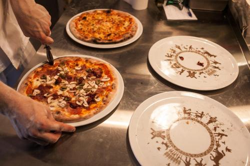 a person cutting a pizza on a table with four plates at Hotel Browar Kościerzyna in Kościerzyna