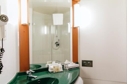 baño con lavabo verde y espejo en ibis Newcastle, en Newcastle