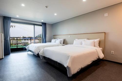 two beds in a hotel room with a balcony at Aewol Stay in Jeju Hotel&Resort in Jeju