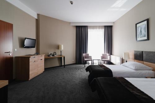 a hotel room with two beds and a desk and a television at Focus Hotel Premium Elbląg in Elblag