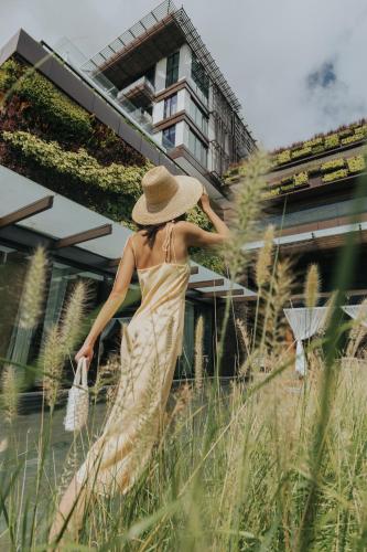 a woman in a straw hat walking through tall grass at 1 Hotel Haitang Bay, Sanya in Sanya