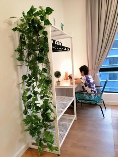 a woman sitting in a chair next to a book shelf with a plant at NORDIC Geniehome2BR1studio Free 90mbps WIFI and Carpark at Utropolis Suite Shah Alam in Shah Alam