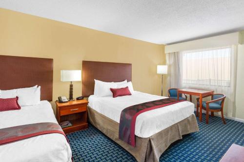 a hotel room with two beds and a desk at Ramada by Wyndham Virginia Beach in Virginia Beach