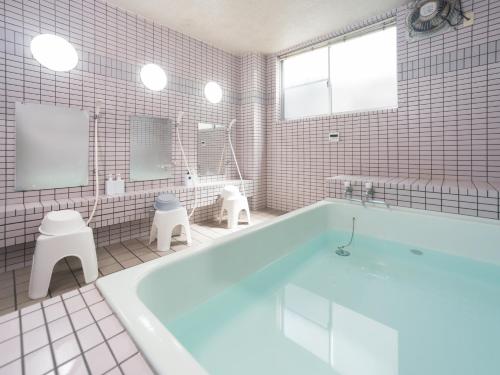 a white bathroom with a tub and a toilet at Tabist Oshiro Ito Tagajo in Tagajo