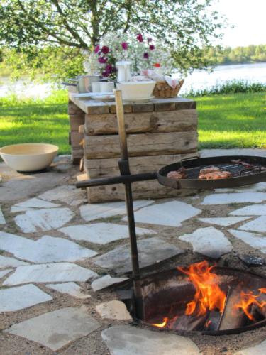 a fire pit on a stone patio with a grill at B&B uniikki majoitus maalaisidyllissä in Tervola
