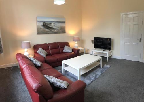 un soggiorno con divano, tavolo e TV di The Station Apartment a Kilmarnock