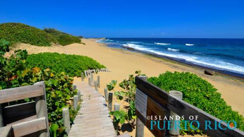 a wooden pathway leading to a beach with a sign at Mar Bonita Beach Apartment in Isabela