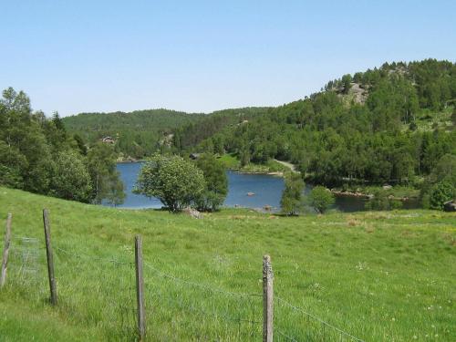 ein Feld mit einem Zaun vor einem See in der Unterkunft 6 person holiday home in lyngdal in Lyngdal