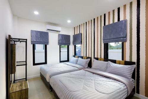 a bedroom with two beds with blue curtains and windows at บ้านซีซ่าเฮ้าส์พูลวิลล่าหัวหิน in Hua Hin
