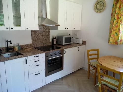 - une cuisine avec des placards blancs, une table et un four micro-ondes dans l'établissement La Petite Grange, à Reynès