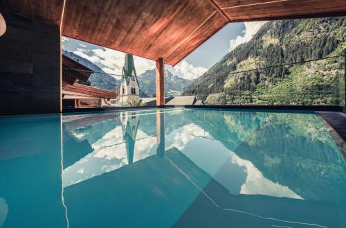 a pool with a view of a church and mountains at Alpenhotel Kramerwirt in Mayrhofen