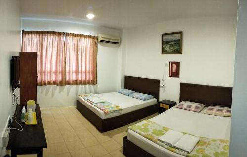a bedroom with two beds and a desk and a window at Hotel Tanjong in Tanjung Malim