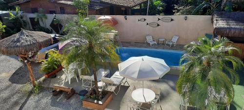 una sombrilla y sillas junto a una piscina con palmeras en Pousada Mar a Pé, en Boicucanga
