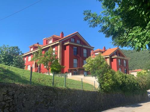 una gran casa roja con una valla delante en Apto Rio Asón Disfruta de la tranquilidad!! Piscina, wifi y parking en Gibaja