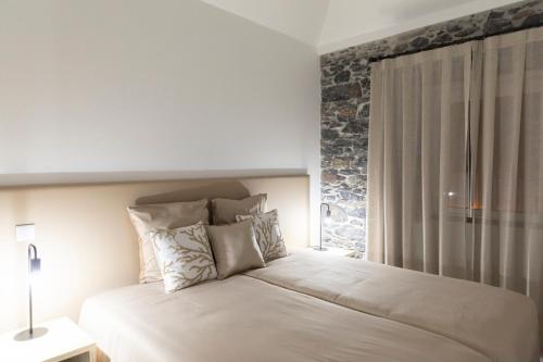 a bedroom with a white bed with a stone wall at Stay in our cozy and wonderful Casa da Rosinha in Arco da Calheta