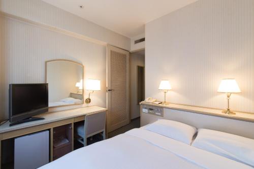 a hotel room with a bed and a desk with a television at Tabist Hotel Tetora Kitakyushu in Kitakyushu