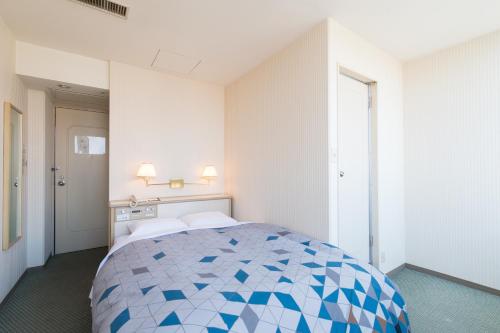 a bedroom with a bed with a blue and white quilt at Tabist Hotel Tetora Kitakyushu in Kitakyushu