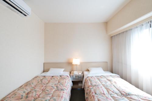 two beds in a small room with a window at Tabist Hotel Tetora Kitakyushu in Kitakyushu