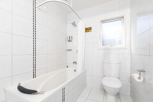 a white bathroom with a tub and a toilet at Beach Street Motel Apartments in New Plymouth