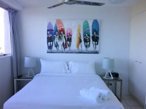 a bedroom with a white bed with surfboards on the wall at Mooloolaba Beachfront Apartment in Sandcastles in Mooloolaba