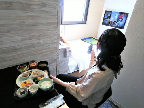 a woman sitting in a room with a tray of food at Hotel AreaOne Nobeoka in Nobeoka