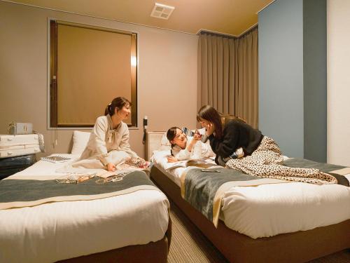 two women and a child sitting on beds in a room at Hotel AreaOne Nobeoka in Nobeoka