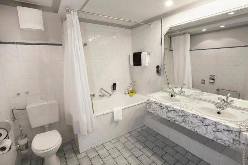 a bathroom with a toilet and a tub and a sink at INA Hotel Royal in Cologne