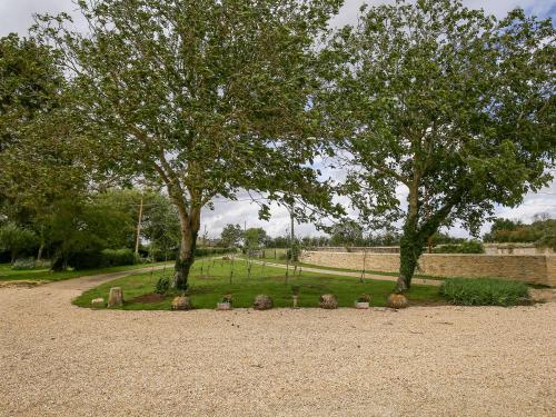a park with two trees and rocks and a wall at Shifford Manor Farm in Witney