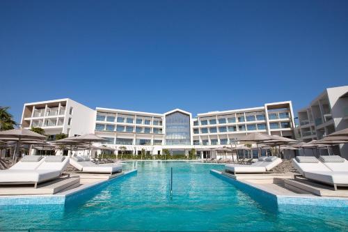 パフォスにあるAtlantica Mare Village Paphosのラウンジチェアとパラソル付きのスイミングプールを併設するホテルです。