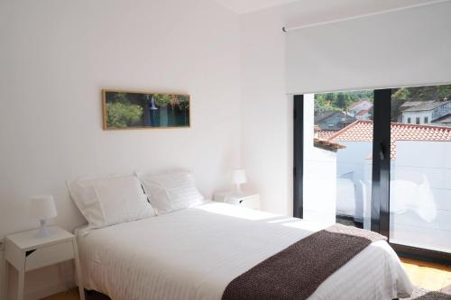 a white bedroom with a bed and a large window at Casa da Ribeira Guesthouse in Alvares