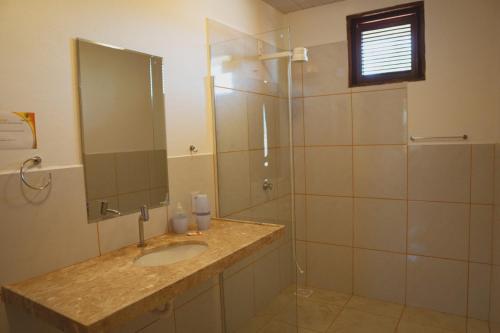 a bathroom with a sink and a shower with a mirror at Hotel Vila Jardim Parajuru in Parajuru