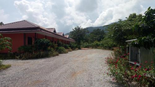 a dirt road next to a red building with flowers at ปันสุขรีสอร์ท in Loei
