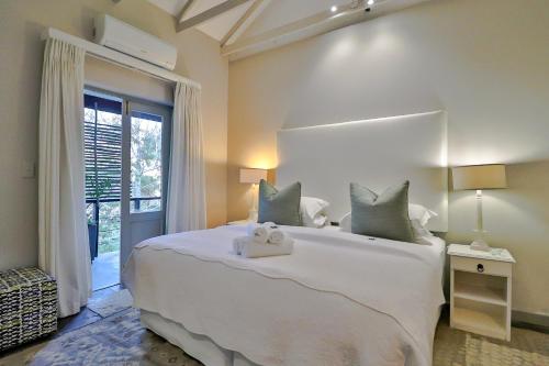 a bedroom with a large white bed with a teddy bear on it at Hermanus Lodge on the Green - Solar Power in Hermanus